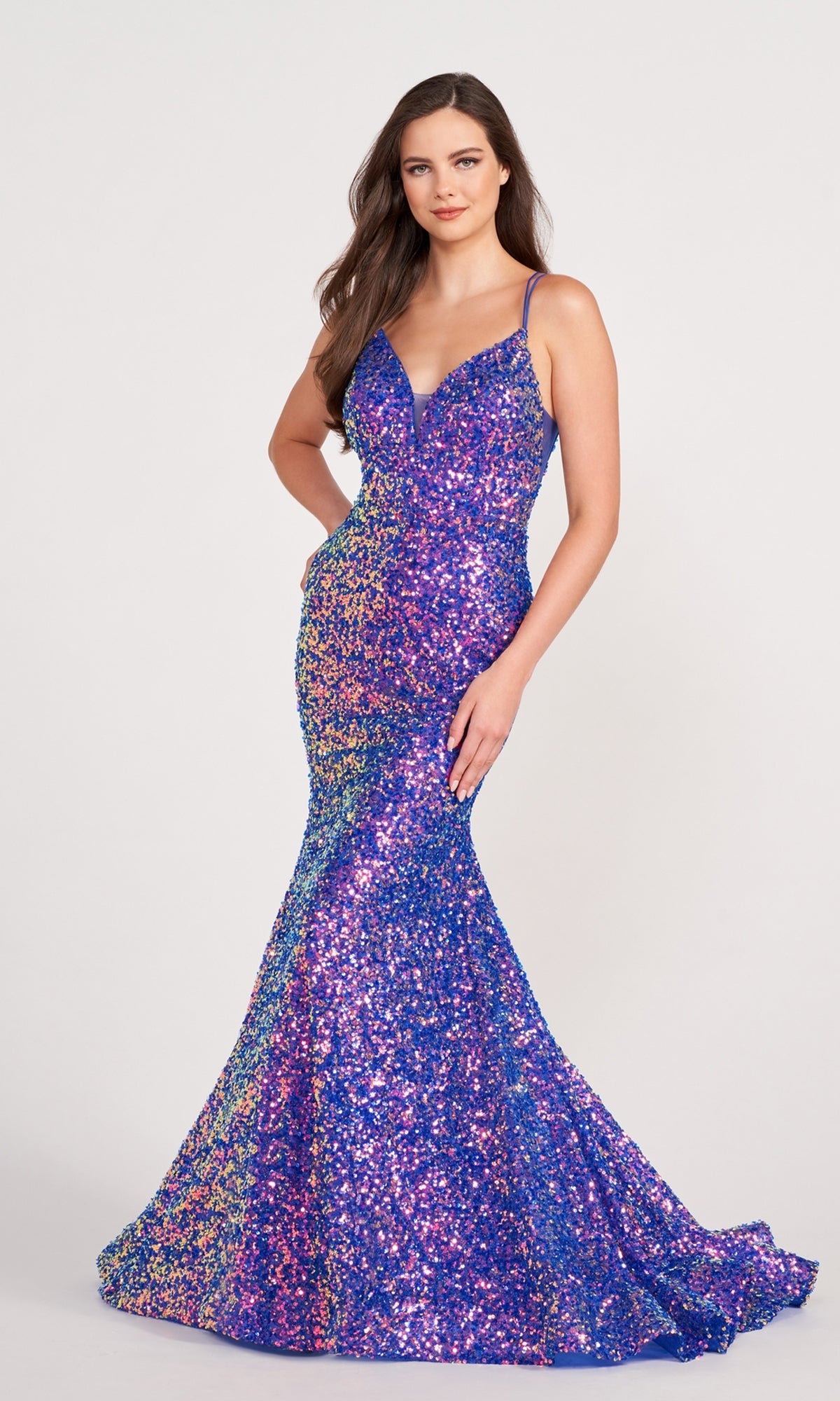 A woman stands against a plain light background wearing an Ellie Wilde Long Stretch-Sequin Prom Dress with a fitted, floor-length design and thin straps.